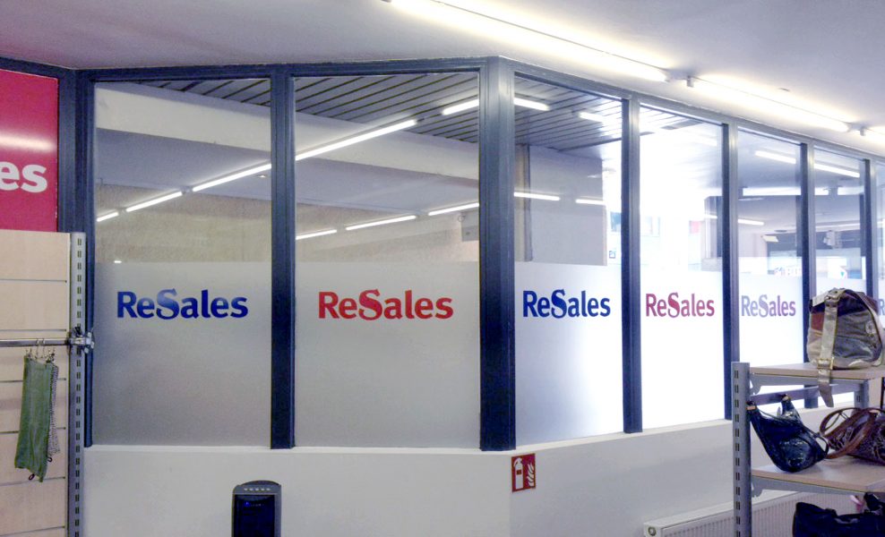 Schaufensterbeklebung für ReSales. Teilfolierung der Scheibe mit Glasdekor und abwechselnd rote und blaue Schriftzüge