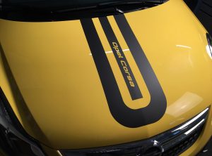 Mit schwarzem Schriftzug Opel Corsa beklebte Motorhaube des gleichnamigen gelben Fahrzeugs