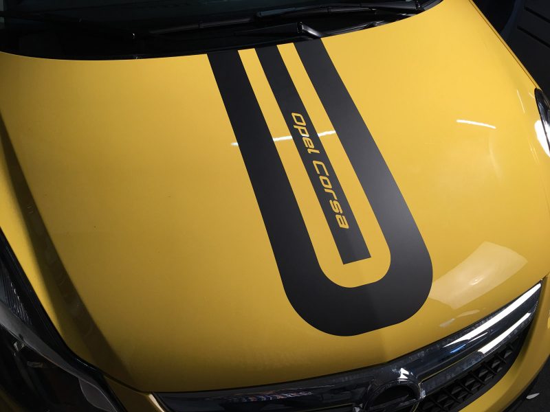 Mit schwarzem Schriftzug Opel Corsa beklebte Motorhaube des gleichnamigen gelben Fahrzeugs