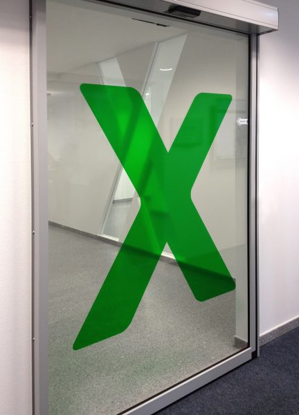 Transluzente Folierung eines großen grünen "X" auf Glasscheibe