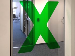 Transluzente Folierung eines großen grünen "X" auf Glasscheibe