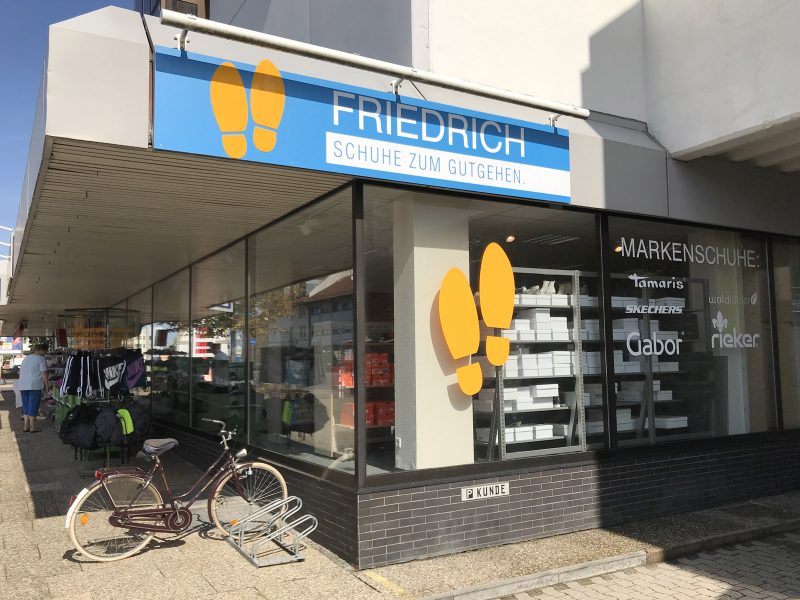 Beklebung - Großes Schild für das Schuhgeschäft Friedrich über dem Schaufenster des Ladens. Zudem sieht man darunter die Folienbeschrifteten Schaufenster
