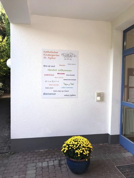 Schilder - Schild auf weißer Hausfassade für den Katholischen Kindergarten St. Xystus in Eingangsbereich