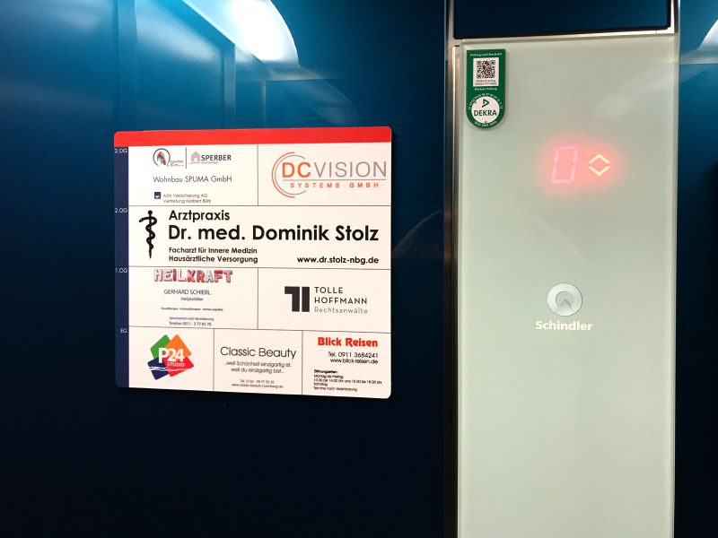 Aufzug-Schild - Aufkleber mit den abgebildeten Firmen in den einzelnen Stockwerken, der an der Wand in einem Aufzug befestigt wurde
