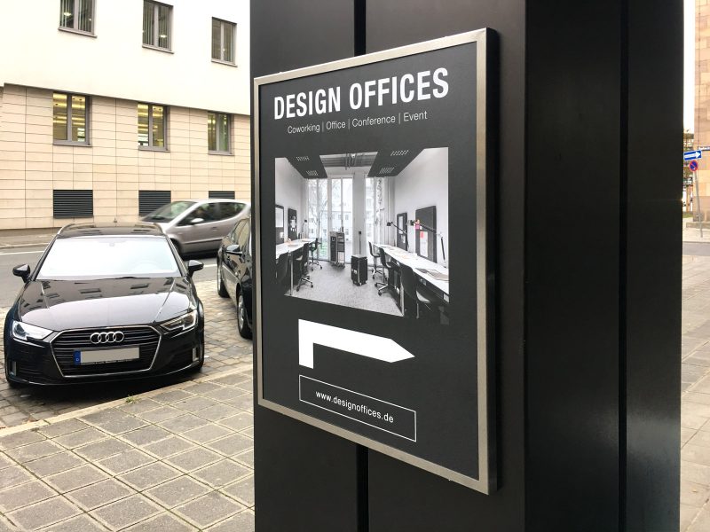 Schilder und Beklebung - Matt gedrucktes Poster in einem Werberahmen für Design Offices, dass an einem breiten Pfosten montiert ist.