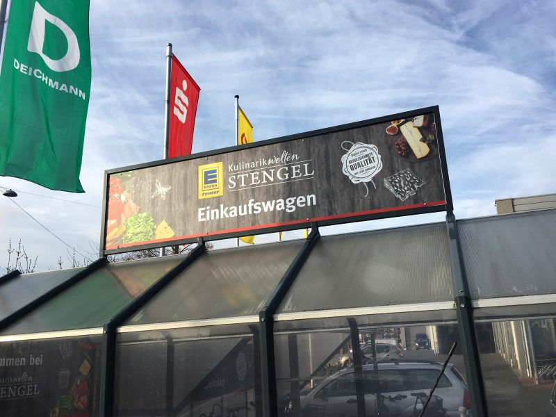 Beklebungsarbeiten - Großes Schild über dem Park-Stellplatz für die Einkaufswagen bei Edeka Stengel