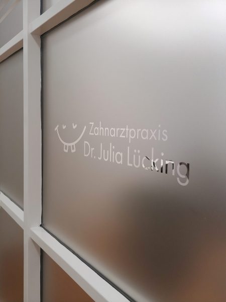 Sichtschutzfolierung - Nahaufnahme einer Glaswand mit Sichtschutzfolie und negativ ausgeschnittenem Logo in der Zahnarztpraxis Lücking in Adelsdorf