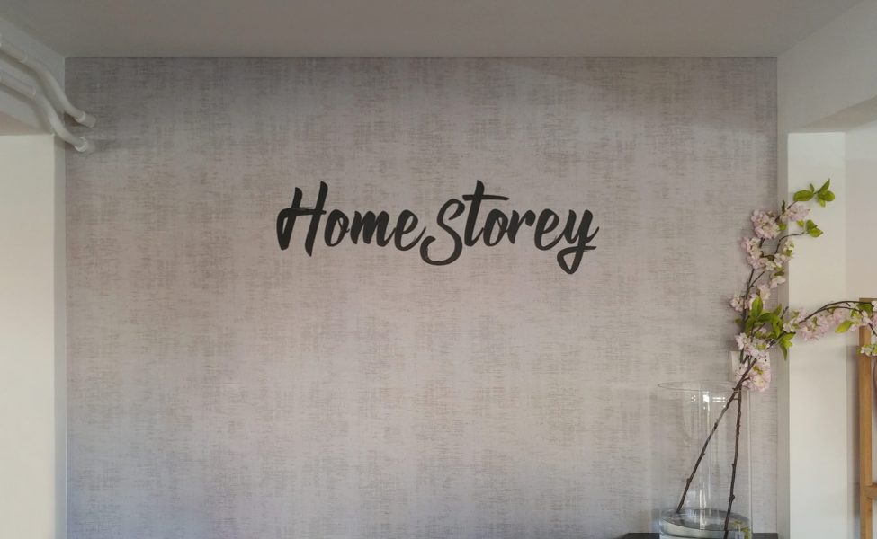Wandtattoo - Home Storey Wandtattoo in schwarzmatt auf einer grauen Tapete