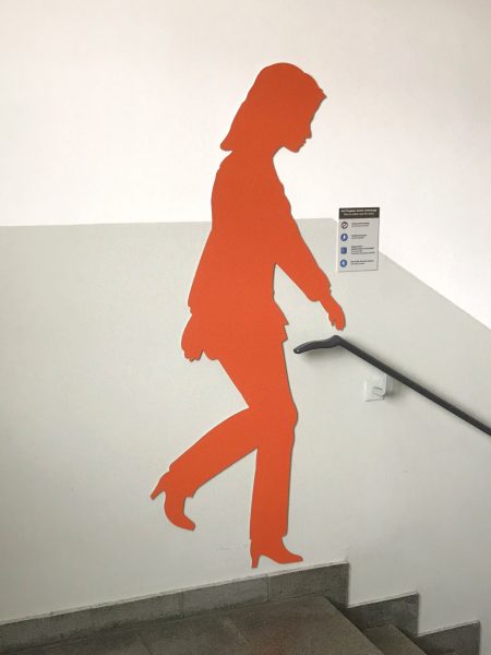 Orangefarbene weibliche Schattenfigur in einem Treppenhaus an der Wand