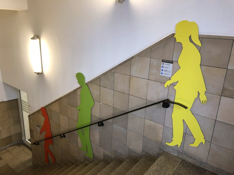 Drei Schattenfiguren in einem Treppenhaus. Jede Figur hat eine andere Farbe.
