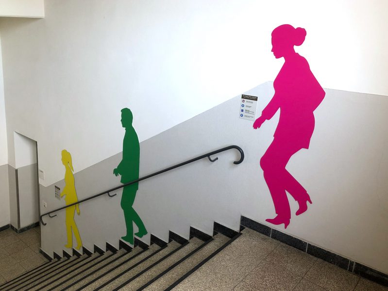 Drei Schattenfiguren in einem Treppenhaus. Jede Figur hat eine andere Farbe.