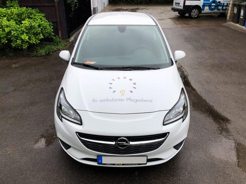 Frontansicht eines neu folierten weißen Opel Corsa für den Spätsommer Pflegedienst