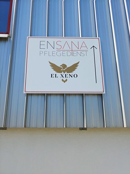 Ein foliertes Firmenschild aus Alu-Dibond an einer Außenwand dient als Wegweiser für den Ensana Pflegedienst und El Xeno
