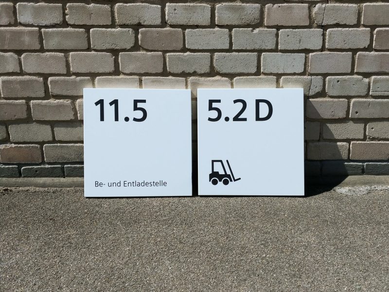 Frontaufnahme aus der Nähe: 2 Schilder mit neuer Folienbeschriftung an eine Mauer gelehnt für Siemens Technopark Nürnberg