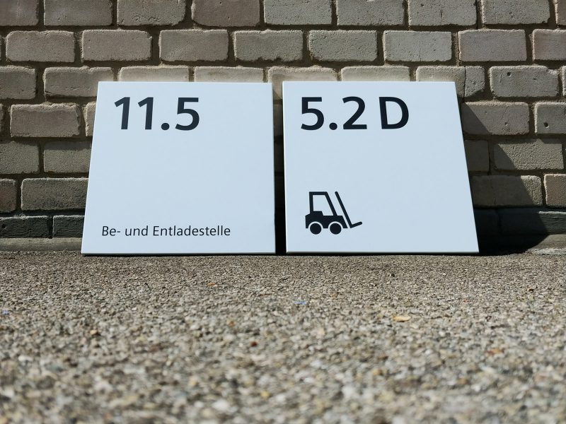 Frontaufnahme von untern: 2 Schilder mit neuer Folienbeschriftung an eine Mauer gelehnt für Siemens Technopark Nürnberg