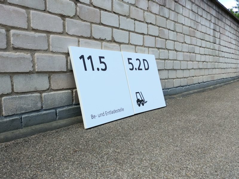 Seitenaufnahme: 2 Schilder mit neuer Folienbeschriftung an eine Mauer gelehnt für Siemens Technopark Nürnberg