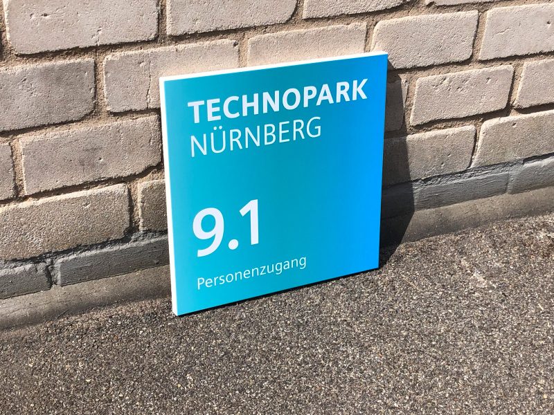 Seitenaufnahme: Ein Schild mit neuer Folienbeschriftung an eine Mauer gelehnt für Siemens Technopark Nürnberg