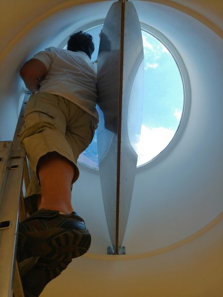 Auf einer Leiter stehender Mitarbeiter von uns der eine Lichtkuppel von innen mit Sonnenschutzfolie beklebt