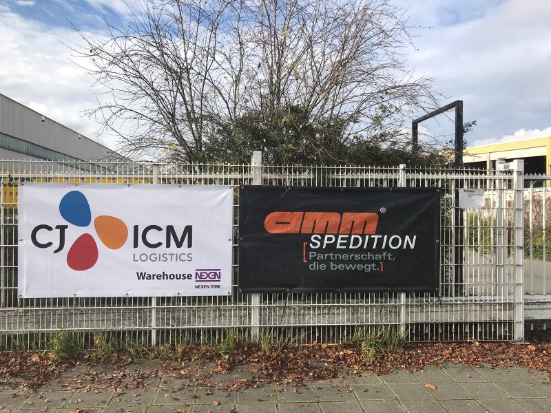 Banner von CJ ICM an einem Zaun befestigt neben einem anderen Firmenschild