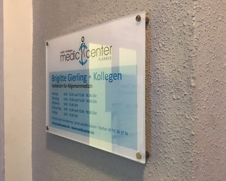Neu foliertes Plexiglasschild mit Edelstahl-Abstandshaltern an der Wand vor dem Eingang zu einer Medic Center Praxis