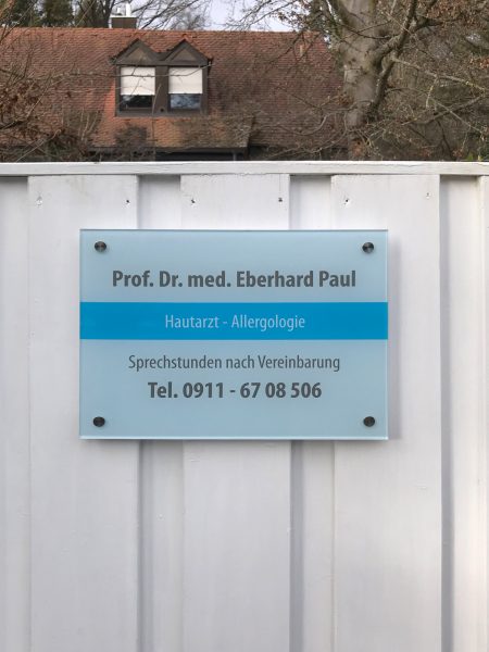 Nahaufnahme: Foliertes Acrylschild am Gartenzaun für den Hautarzt Prof. Dr. med. Eberhard Paul