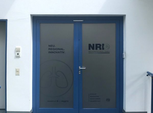 Firmenbeschilderung - Sichtschutzfolierung mit Logos an Eingang für das NRI