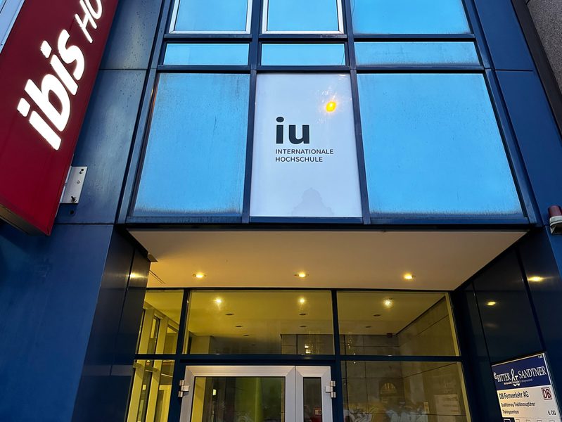 Campusfolierung an der IU in Nürnberg - Außenschild mit IU Logo über Eingang auf Fensterscheibe